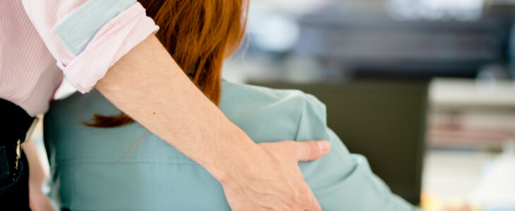 Rear view of a male manager sexually harassing a female colleague working on a laptop in an office
