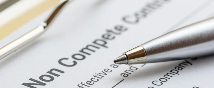 A close-up of a "Non Compete Contract" document with a silver pen resting on it.