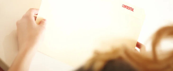 A person holding a manila folder stamped "CONFIDENTIAL".